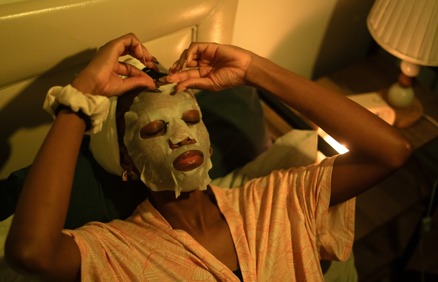 A woman applies a sheet mask in bed.