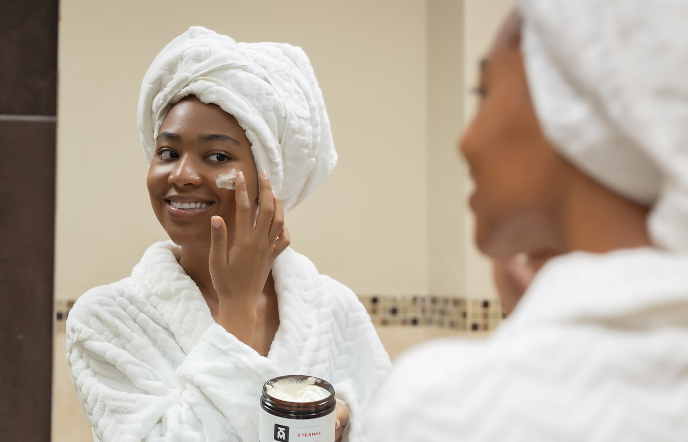 a woman with a towel on her head and a jar of cream on her face