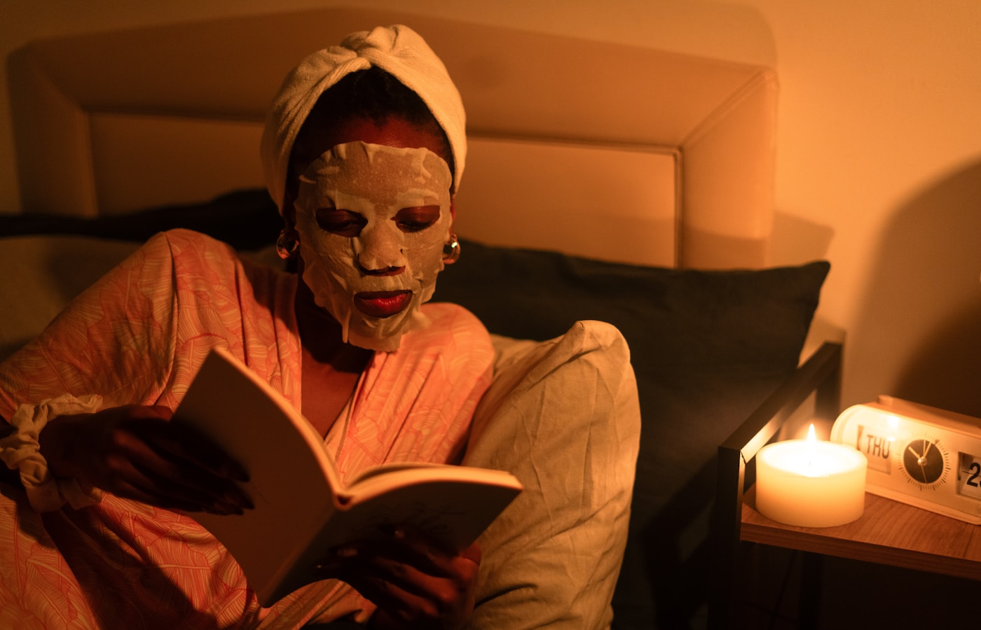 Woman with face mask reads book in dimly lit room.
